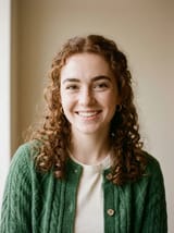 Portrait photo of a smiling young woman with curly auburn hair, freckles and a green knit cardigan